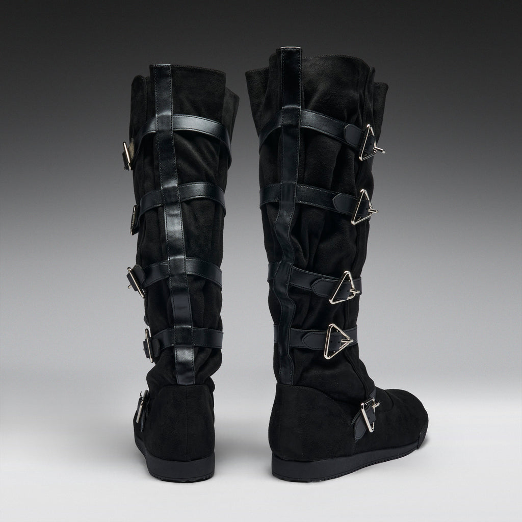 A pair of black knee-high boots with multiple black leather straps and silver-tone triangular metal buckles, shown from the back on a gray gradient studio background.