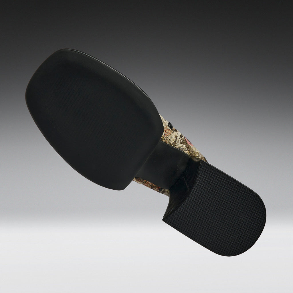 A black motorcycle or bicycle handlebar grip cover with a textured black rubber face and a camouflage-patterned stem section, shown against a dark gray gradient background.
