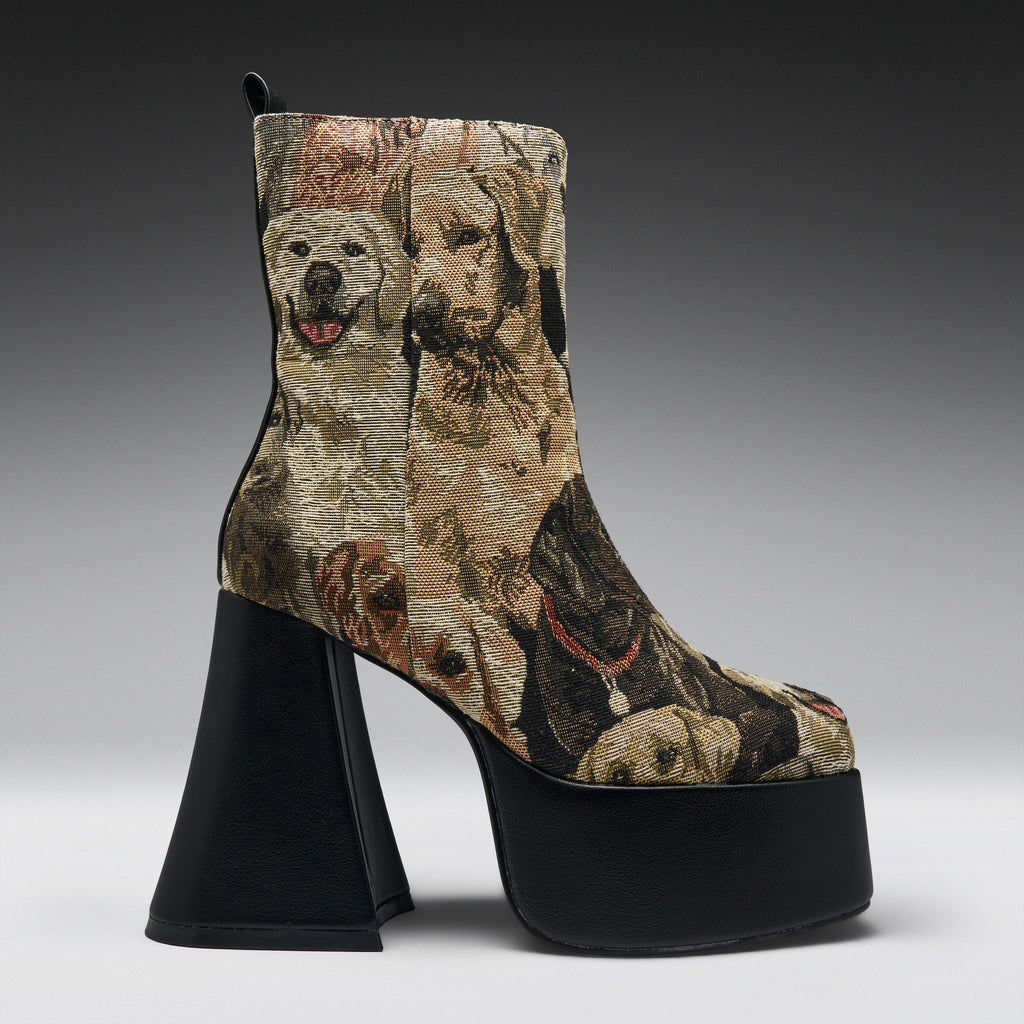 A high-heeled ankle boot with a black platform sole and block heel, featuring a woven or printed pattern of various dog portraits in beige, brown, and black tones.