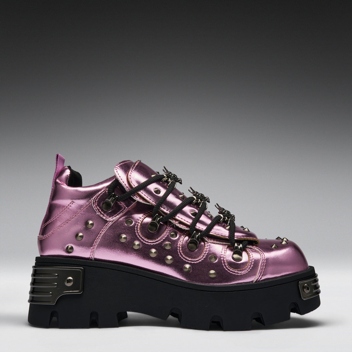 A metallic pink platform sneaker with black laces, silver studs, and a chunky black sole, shown from a side profile on a gray gradient background.