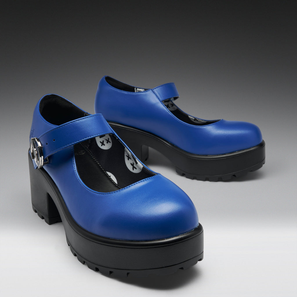 A pair of blue Mary Jane platform shoes with black block heels and soles, featuring silver buckle details and white star-and-circle patterns on the straps, shown on a dark-to-light gray gradient background.