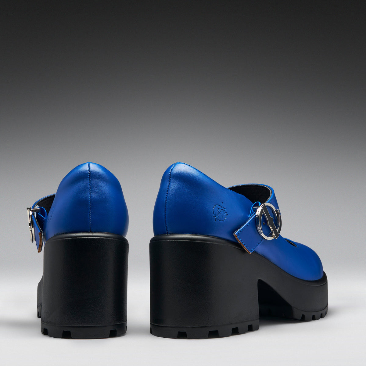 A pair of Mary Jane-style platform heels shown from the back, featuring a vibrant blue leather upper with a silver-tone ring detail and a chunky black platform sole.
