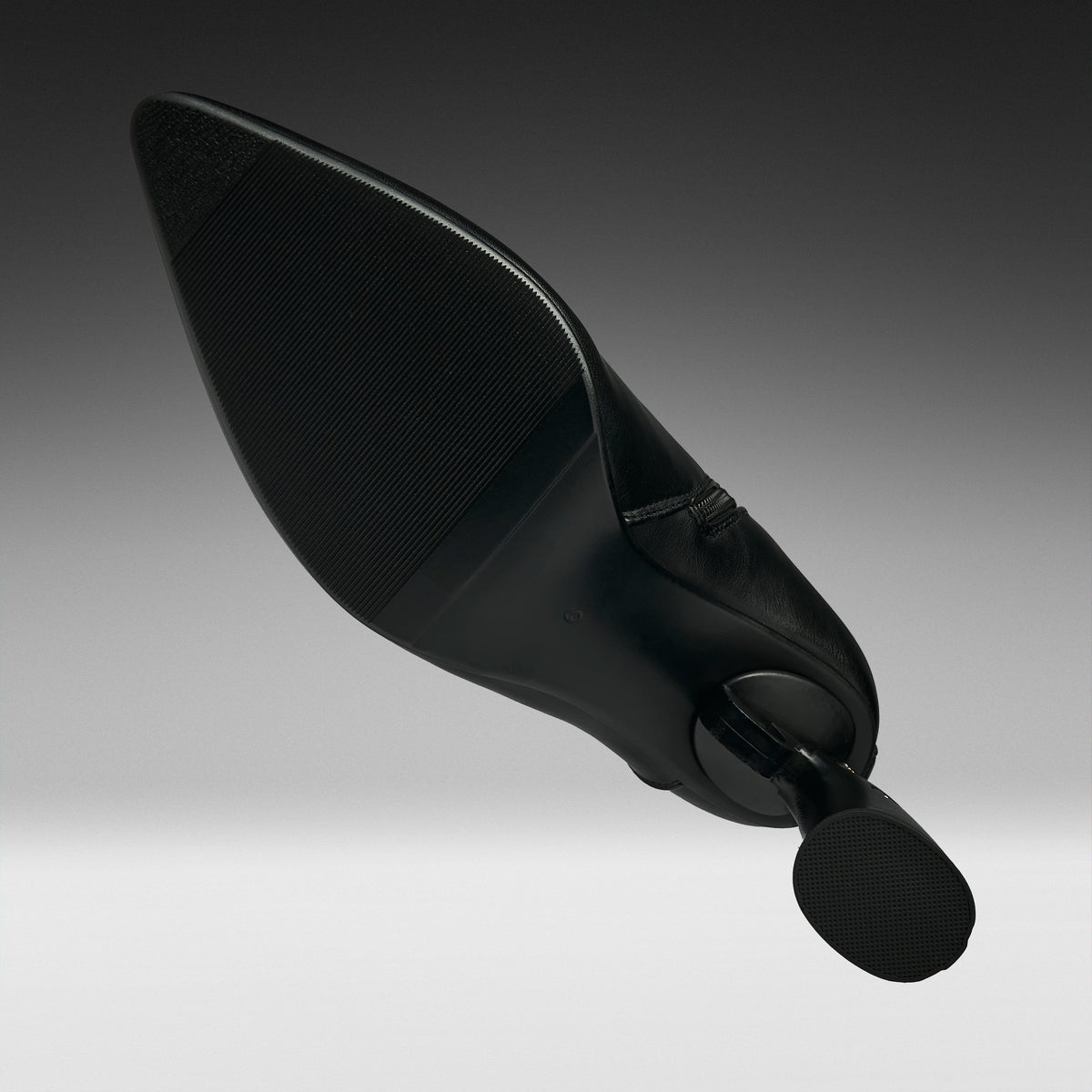 A black pointed-toe stiletto heel shoe shown from a dramatic angled perspective against a dark-to-light gray gradient studio background.