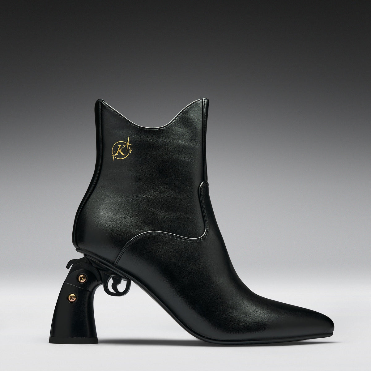 A black leather ankle boot with a pointed toe, a unique pistol-shaped block heel, and a gold Karl Lagerfeld logo on the side, shown against a dark gray gradient background.