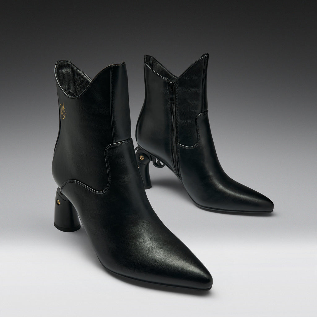 A pair of black leather ankle boots with pointed toes and block heels, displayed on a clean gray gradient studio background.