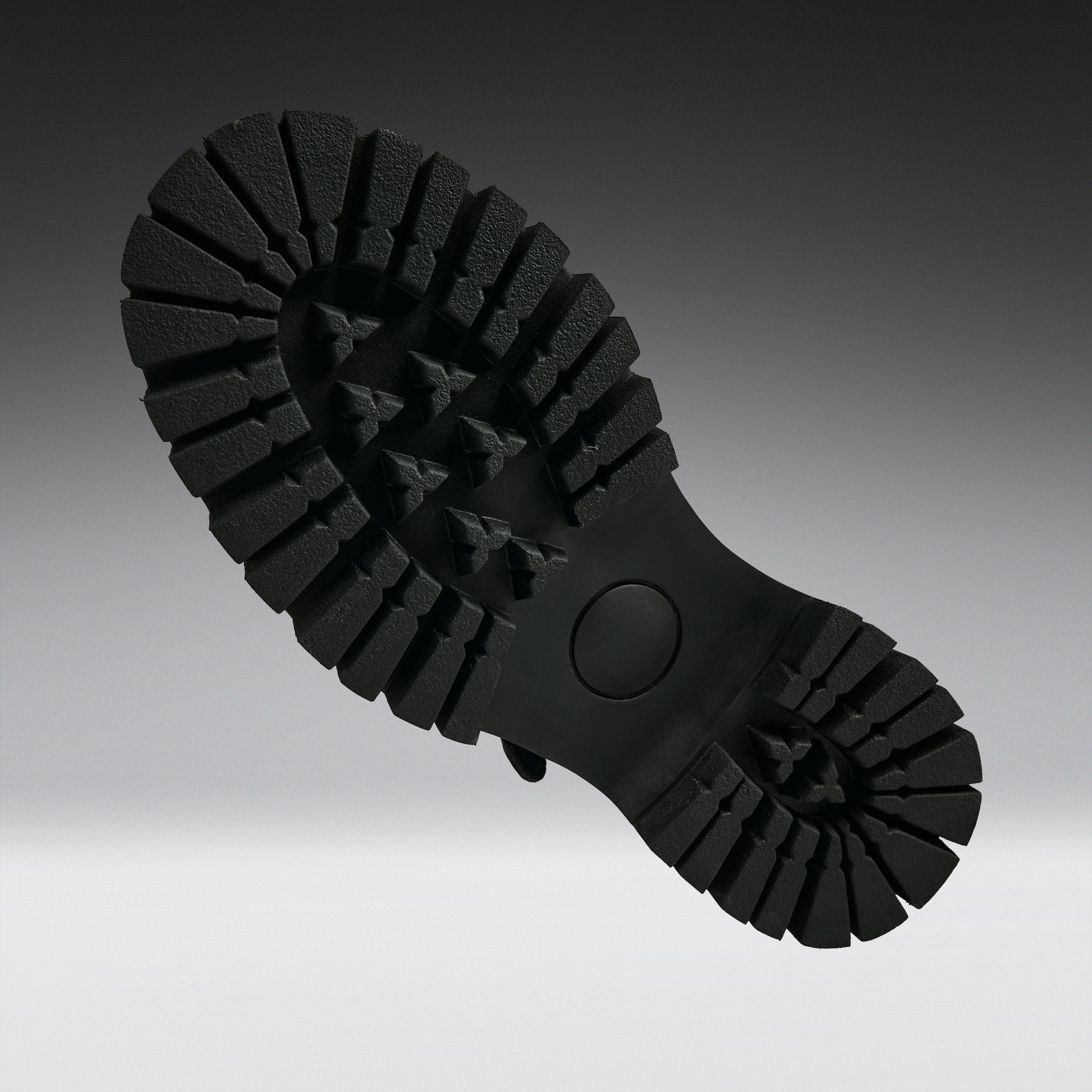 A close-up of a black rubber shoe sole, showing the deep lugs and tread pattern, photographed against a dark-to-light gray gradient background.